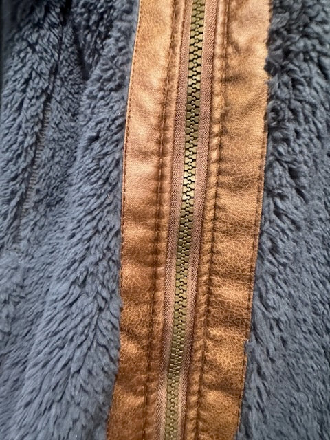Close-up of a navy fleece jacket with a vertical tan faux-leather zipper panel and a gold-tone metal zipper.